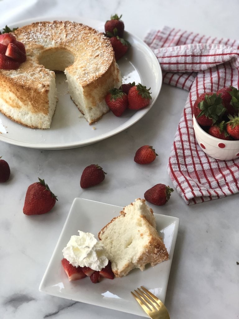 gluten-free angel food cake with slice topped with strawberries and whipped cream