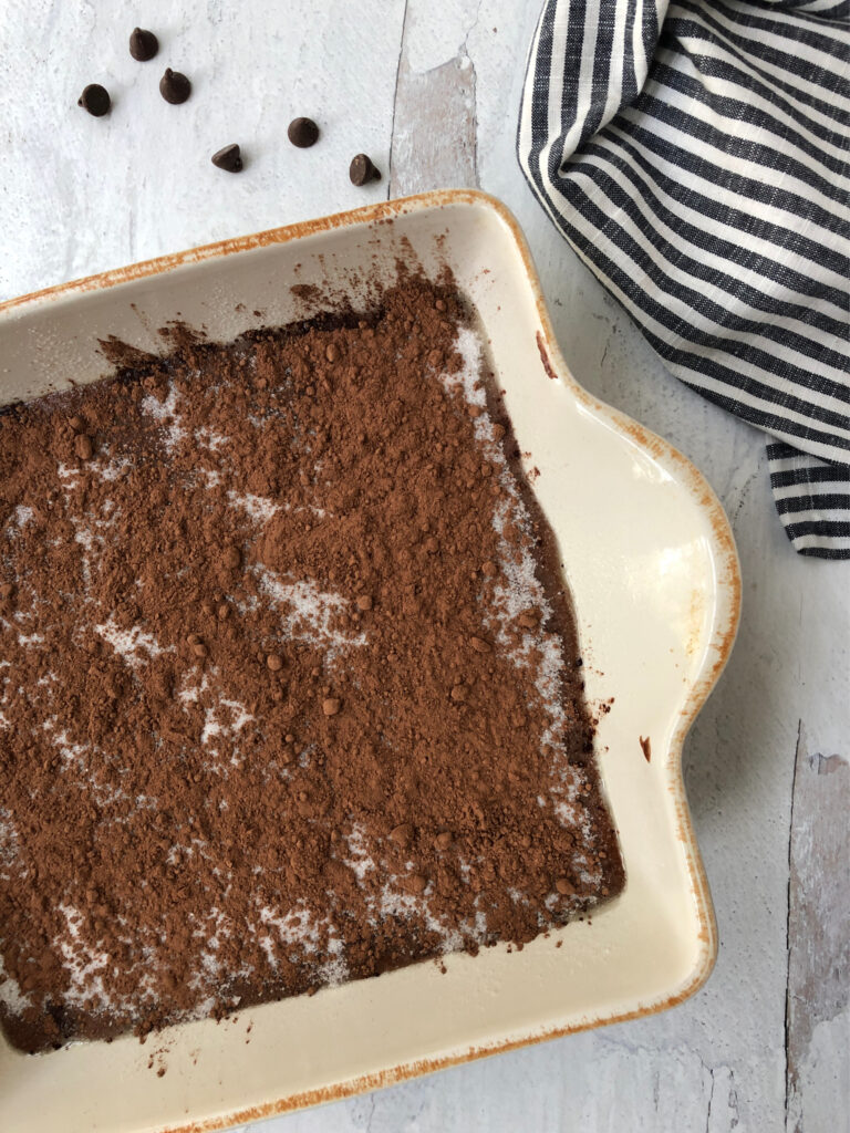 Pudding cake batter inside square baking dish topped with sugar and cocoa