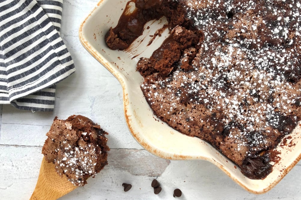 Overhead picture of pudding cake with powdered sugar and a scoop of it on a wooden spoon