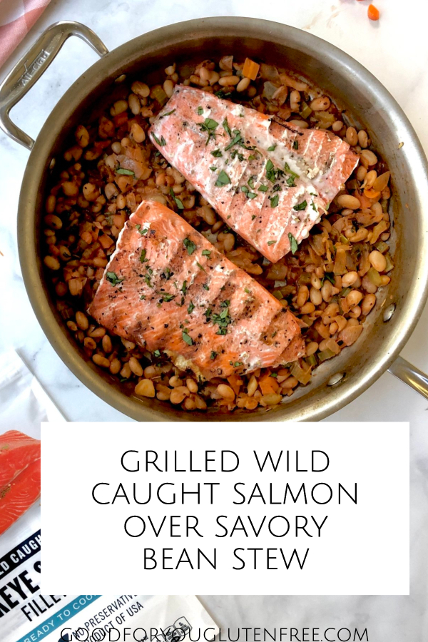 Pin image featuring two cooked wild salmon fillets served over the bean stew inside a large saute pan.