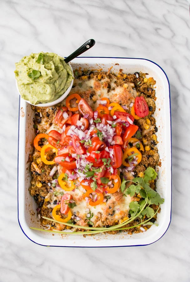 Picture of quinoa in a casserole dish topped with melted cheese, peppers, red onions, cilantro and a side of guacamole. Recipe by My Kitchen Love