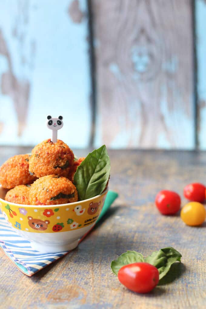 Bowl of cheese and tomato quinoa balls with a toothpick in the center of one by Healthy Little Foods.