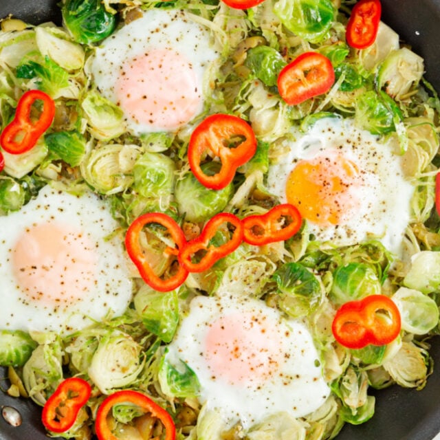 upclose picture of cooked eggs inside skillet with brussel sprouts and topped with red peppers