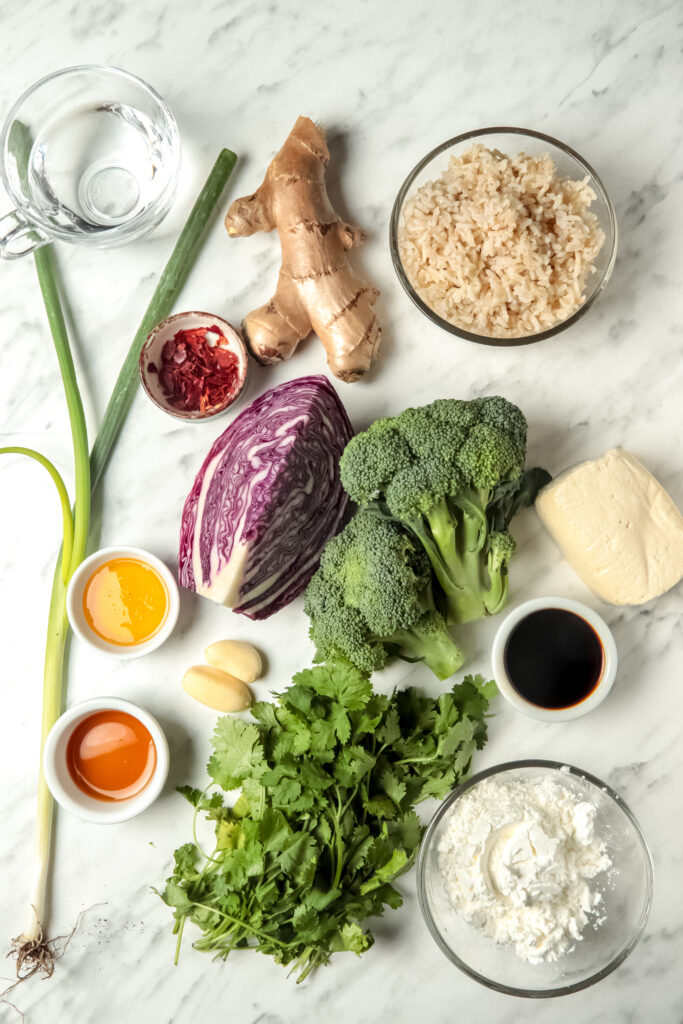 Picture of ingredients used to make crispy tofu stir-fry including tofu, cornstarch, broccoli, purple cabbage, garlic, cilantro, ginger and oil.
