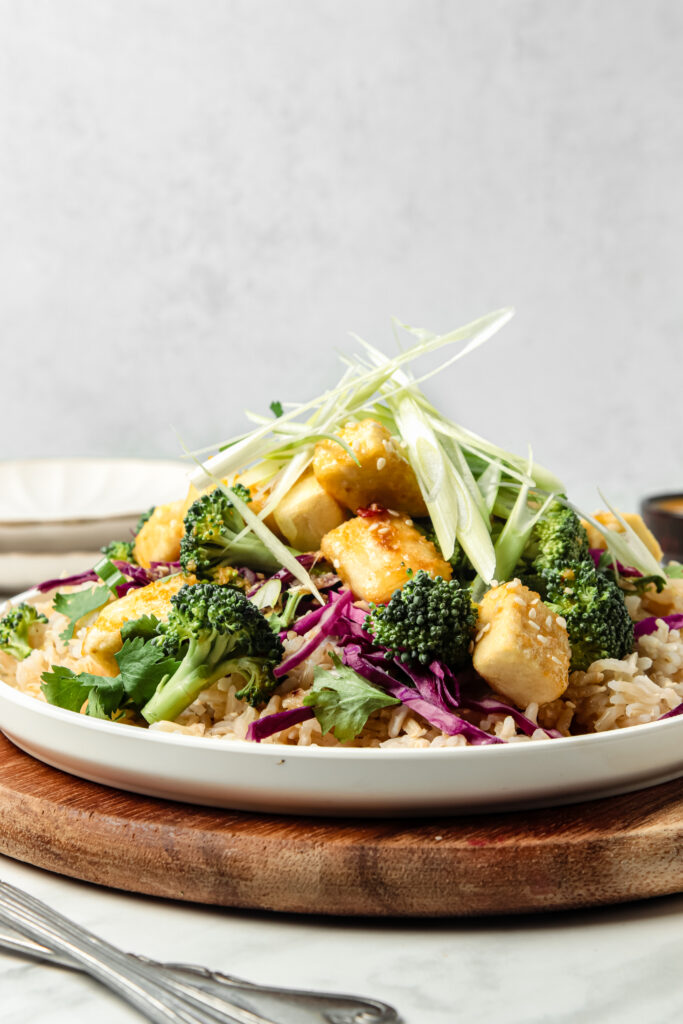 Side image of the crispy tofu stir-fry on a plate and topped with green onions and sesame seeds