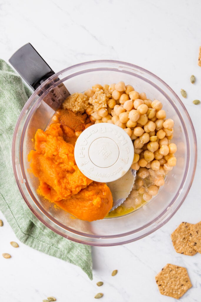 Food processor with garbanzo beans, pumpkin puree and other ingredients needed for hummus recipe.