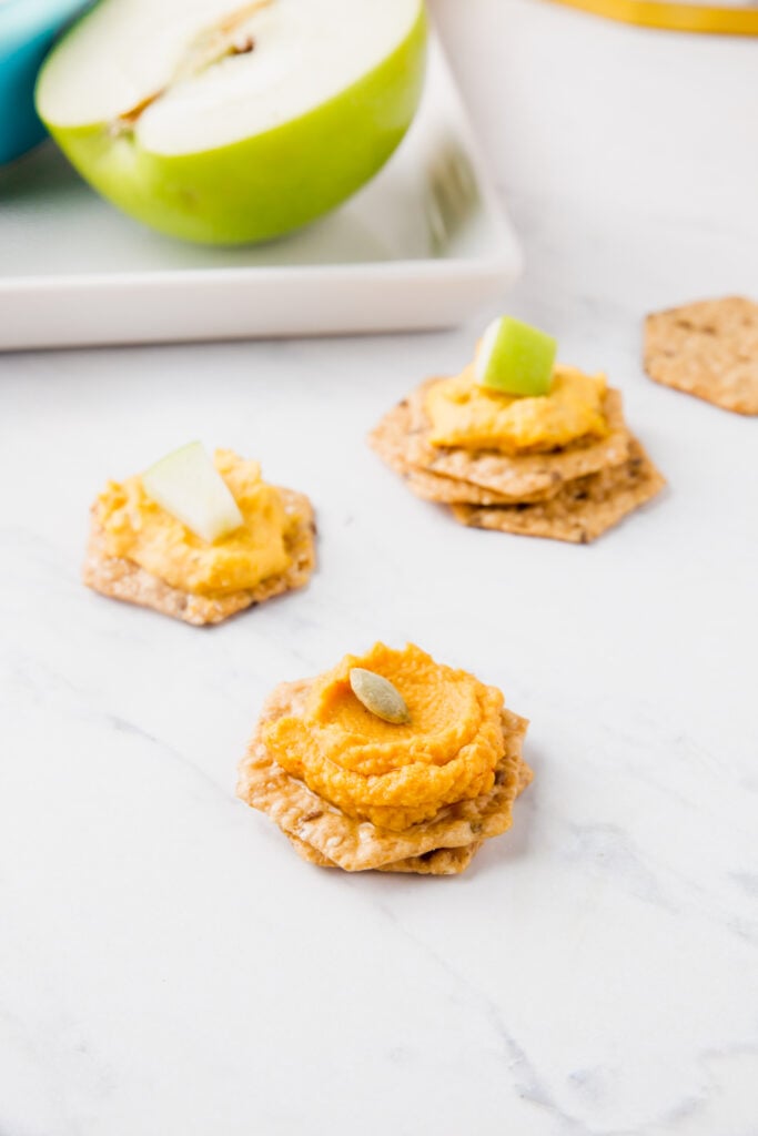 Crackers topped with pumpkin hummus dip and pumpkin seeds