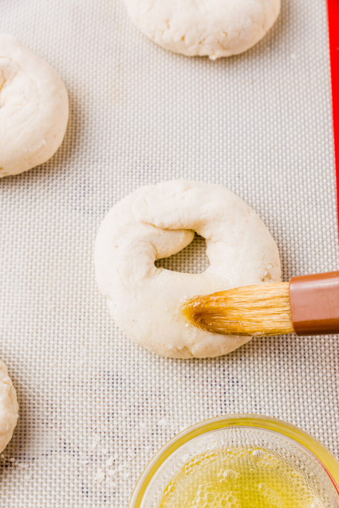 Dough formed into bagel shape and being brushed with egg white