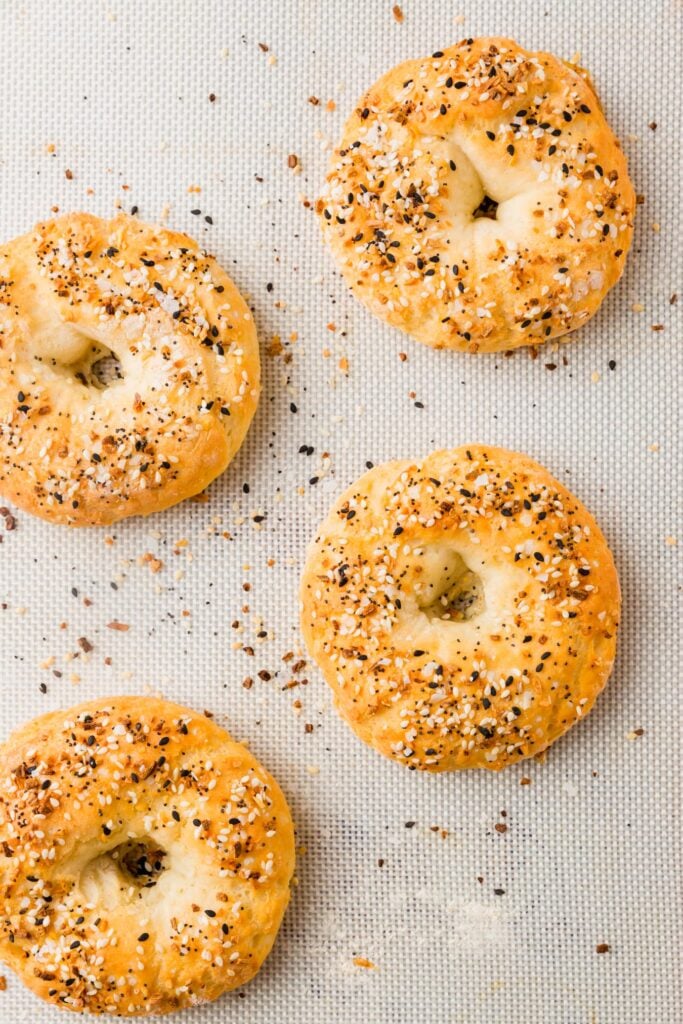 Picture of four browned gluten-free bagels on a silpat mat. Bagels are topped with everything bagel seasoning