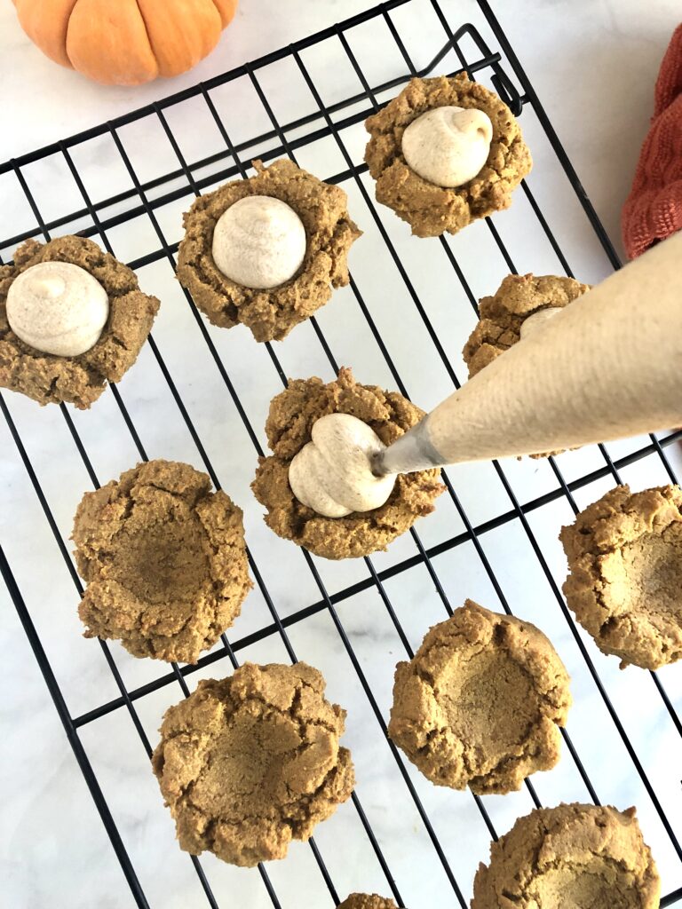 Using a piping bag of frosting to add frosting to the middle of the cassava flour pumpkin cookies