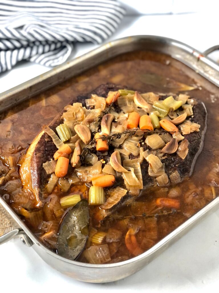 Picture of cooked beef brisket in casserole dish with all the drippings surrounding it.