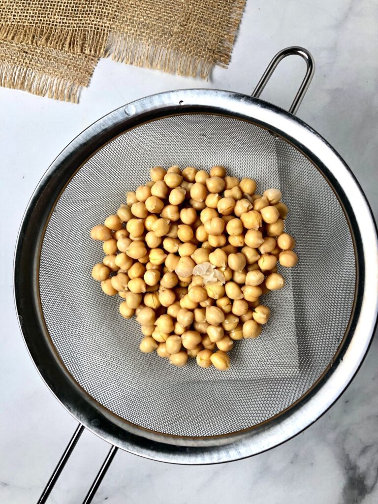 Picture of garbanzo beans in a strainer and the skins coming off of some of them.
