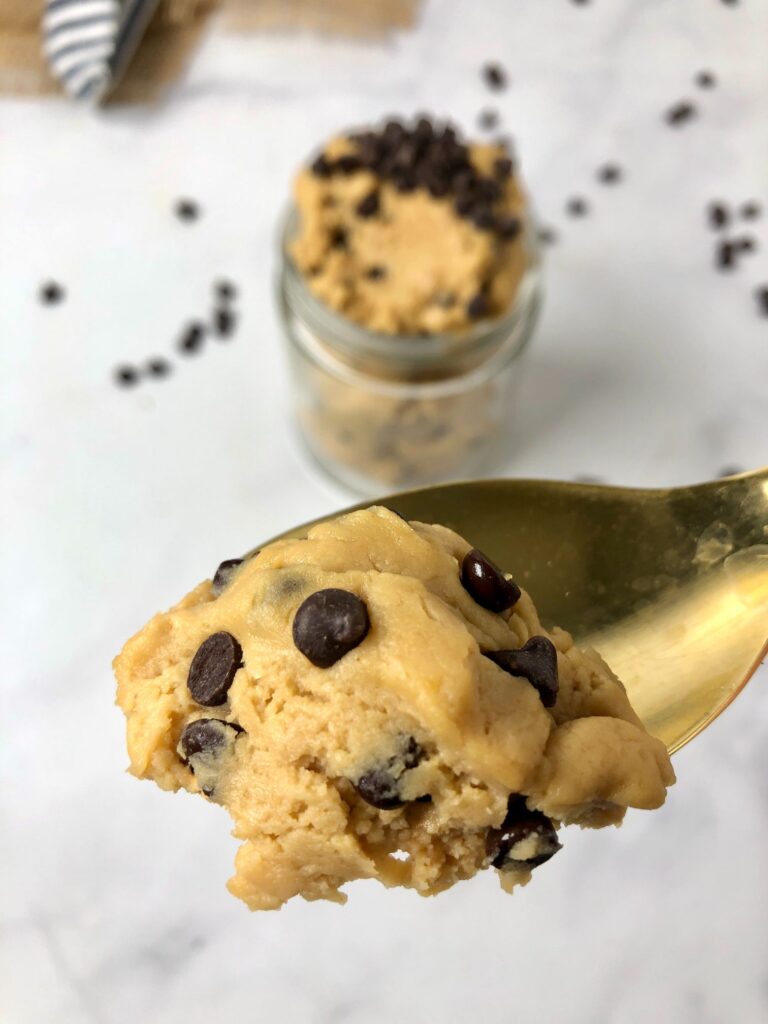 Upclose image of edible cookie dough on a spoon with jar of dough in background
