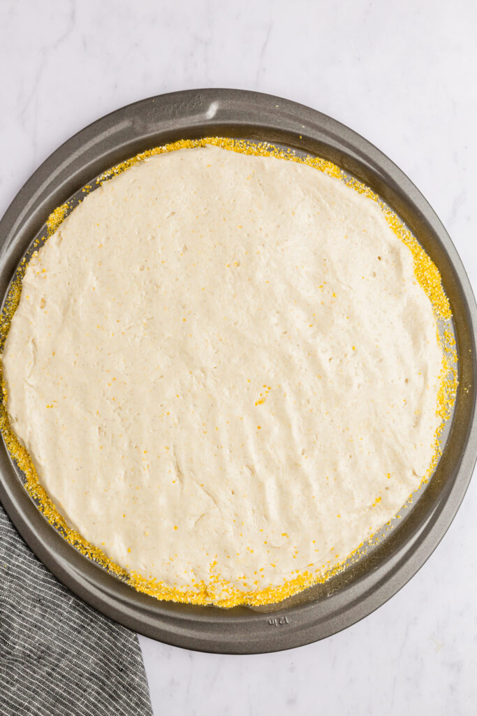 Picture of pizza dough on a pizza tray with polenta or corn grits on the bottom