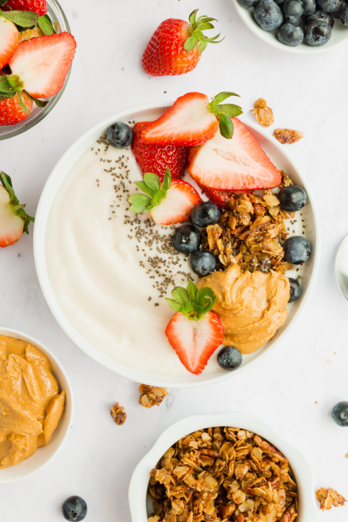 Upclose picture of make your own yogurt bowl topped with strawberries, blueberries, granola, peanut butter and chia seeds.