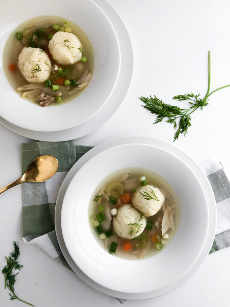 two bowls of matzo ball soup topped with scallions and dill