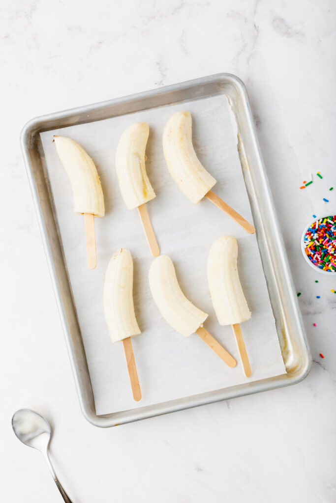 Frozen banana with popsicle sticks on a baking tray
