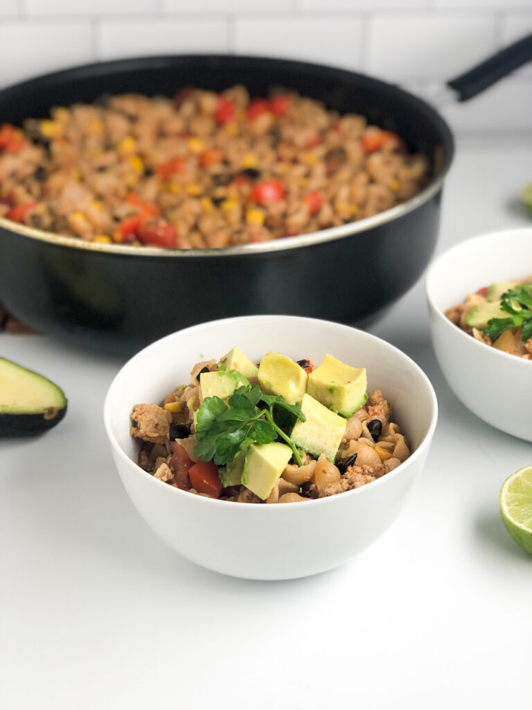 up close on bowl of taco pasta skillet topped with cilantro and avocados