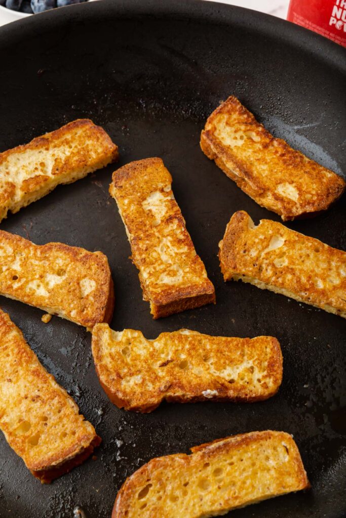 gluten-free french toast sticks cooking in a skillet and turning golden brown