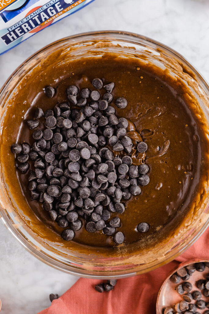 adding chocolate chips to brownie batter in a bowl