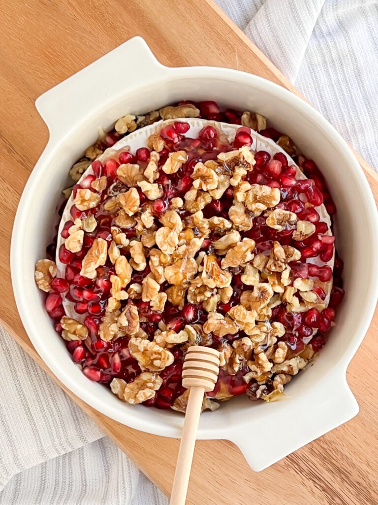 brie cheese round topped with pomegranate arils, walnuts and honey
