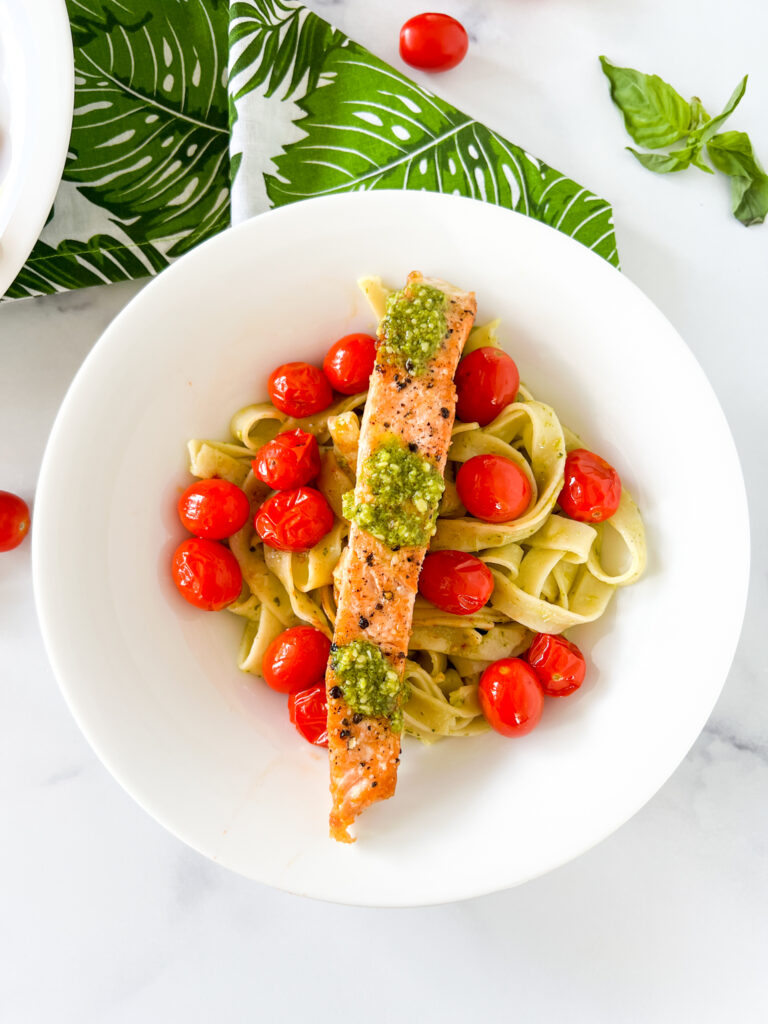 salmon pesto pasta served in a bowl with  blistered grape tomatoes