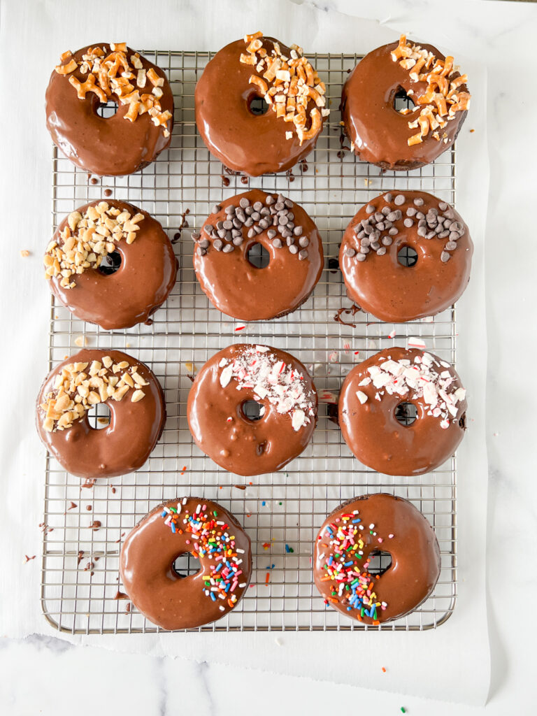 gluten-free chocolate donuts with chocolate glaze and various fun toppings on top of a wire rack