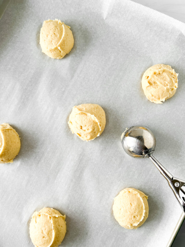 cookie dough balls with cookie scooper on baking sheet