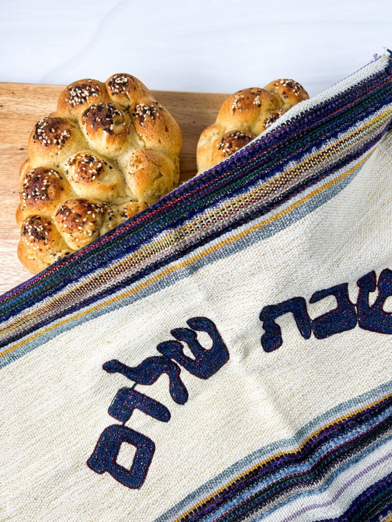 challah covered with challah cover that says Shabbat Shalom in Hebrew