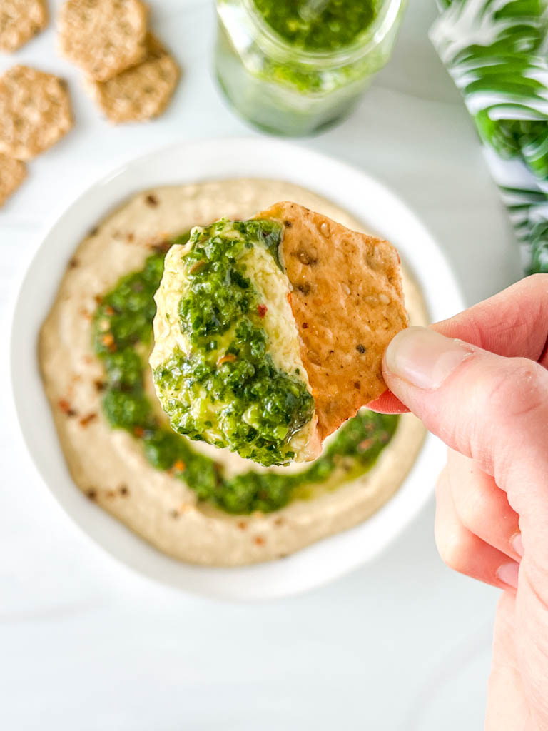 upclose on crunchmaster cracker dipped in zhoug-topped hummus